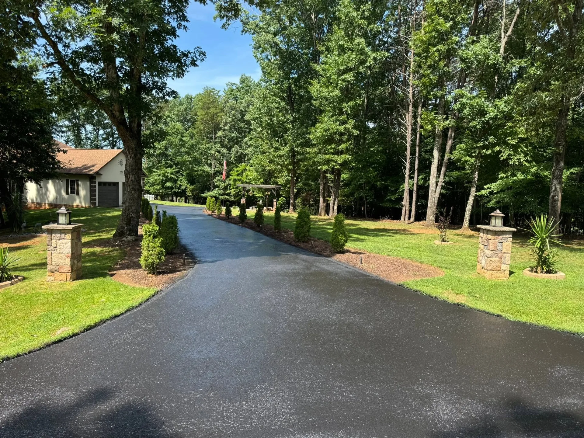 Freshly paved tree-lined driveway entrance by Driveway Pros